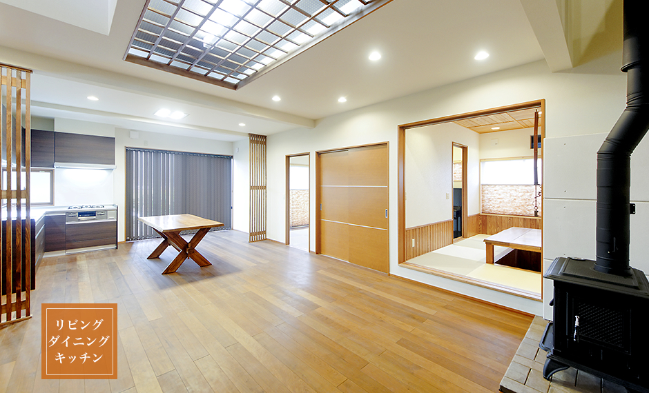 カバザクラの床材、タモの敷居、食器棚や冷蔵庫の目隠しなど、木の種類により特徴を生かしたLDK。薪ストーブの温かい空気が流れるダイニングには職人作のテーブル。木の梁などを表面に出せない天井は凸凹段差やオリジナル照明で空間演出。
